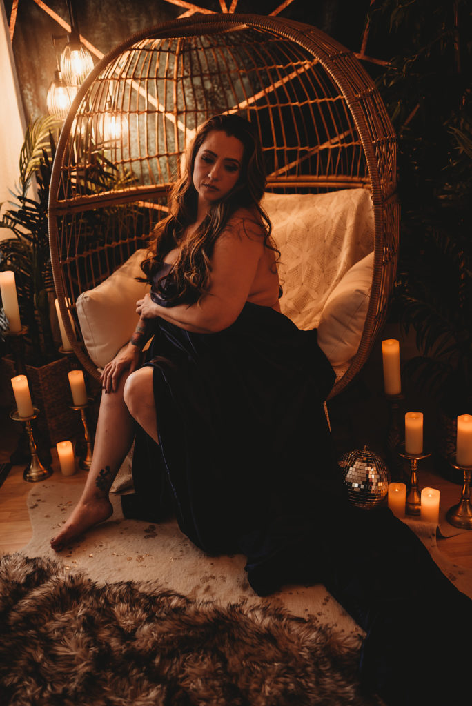 Folsom boudoir session in egg chair with satin sheet and cozy, feminine energy